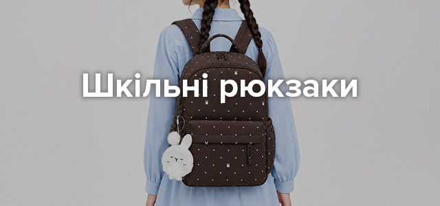 Категорійний банер «Шкільні рюкзаки»: дівчина у сірому с світшоті та джинсах тримає бежево-коричневий шкільний рюкзак із брелоком-іграшкою