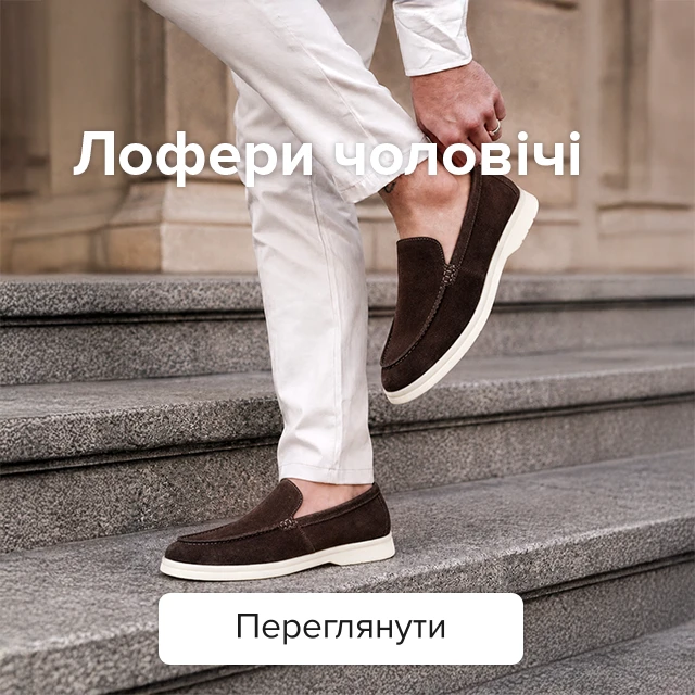 Категорійний банер «Лофери чоловічі»: чоловік у білих штанах та темно-коричневих замшевих лоферах із білою підошвою стоїть на кам'яних сходах