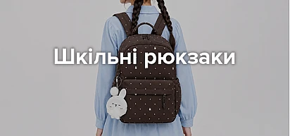 Категорійний банер «Шкільні рюкзаки»: дівчина у сірому с світшоті та джинсах тримає бежево-коричневий шкільний рюкзак із брелоком-іграшкою
