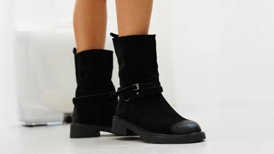 Жіночі чорні замшеві чоботи на низькому ходу з декоративним ремінцем і шкіряним носком, вид збоку на моделі