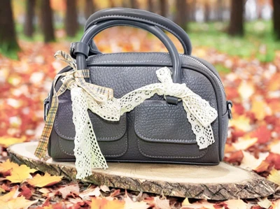 Женская сумка из эко-кожи графитового цвета с кружевными бантами на фоне осеннего парка