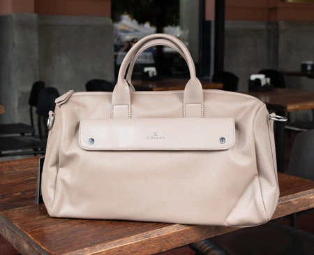 Жіноча бежева шкіряна сумка з короткими ручками на дерев'яному столі