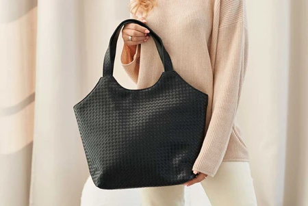 Большая черная женская сумка-шоппер из фактурной экокожи в руке женщины в светлом свитере